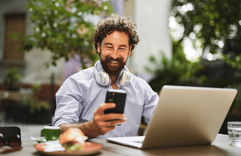 Man looking at phone while working on laptop